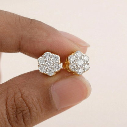 Gold earrings with diamond-like stones held between fingers against a beige background