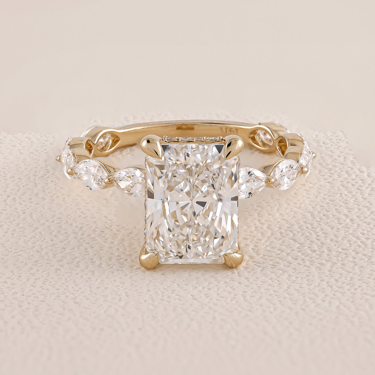 Gold ring with a large diamond and smaller diamonds on the sides on a beige fabric background