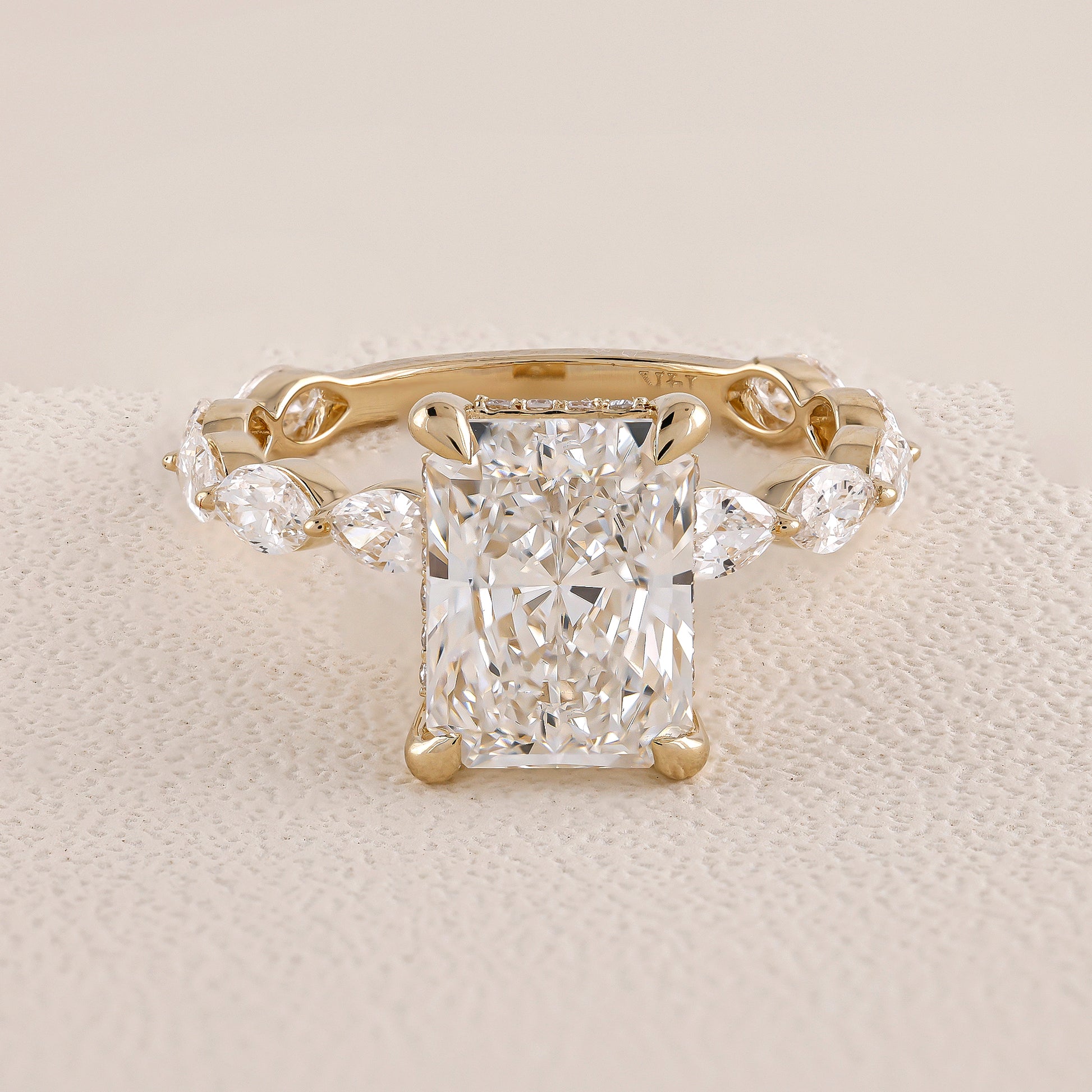 Gold ring with a large diamond and smaller diamonds on the sides on a beige fabric background