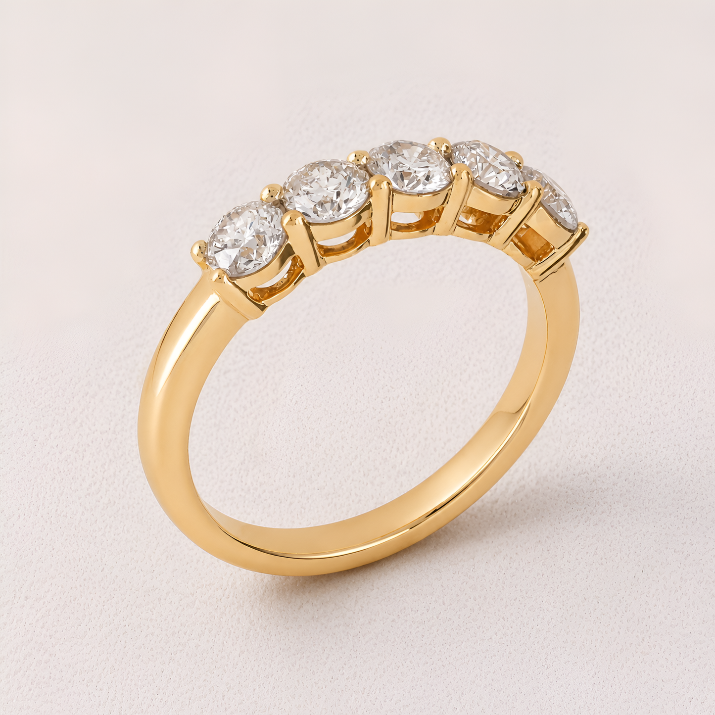 A yellow gold ring with five round-cut clear gemstones in a half-circle setting, photographed on a light beige background.