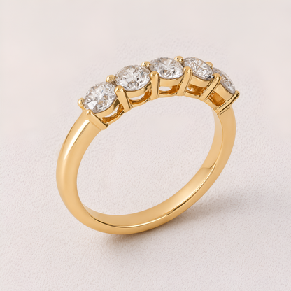 A yellow gold ring with five round-cut clear gemstones in a half-circle setting, photographed on a light beige background.