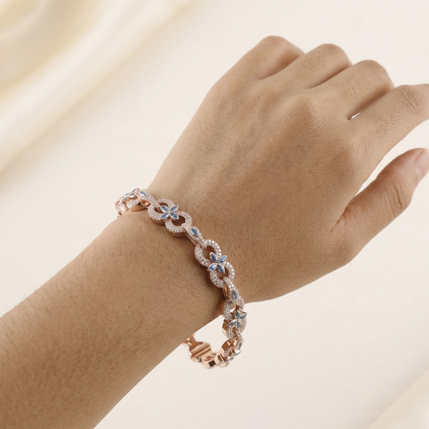 Rose gold bracelet with blue stones on a wrist against a beige background