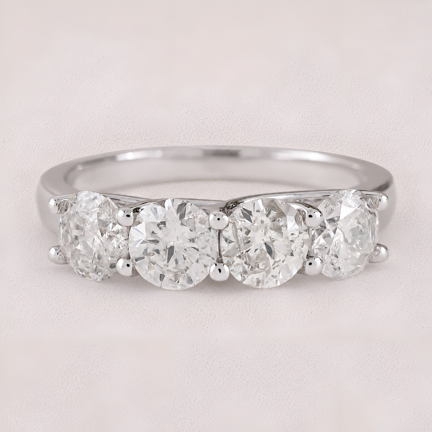 A three-stone diamond ring with round-cut diamonds set in a polished silver-colored band, shown on a light beige textured background.