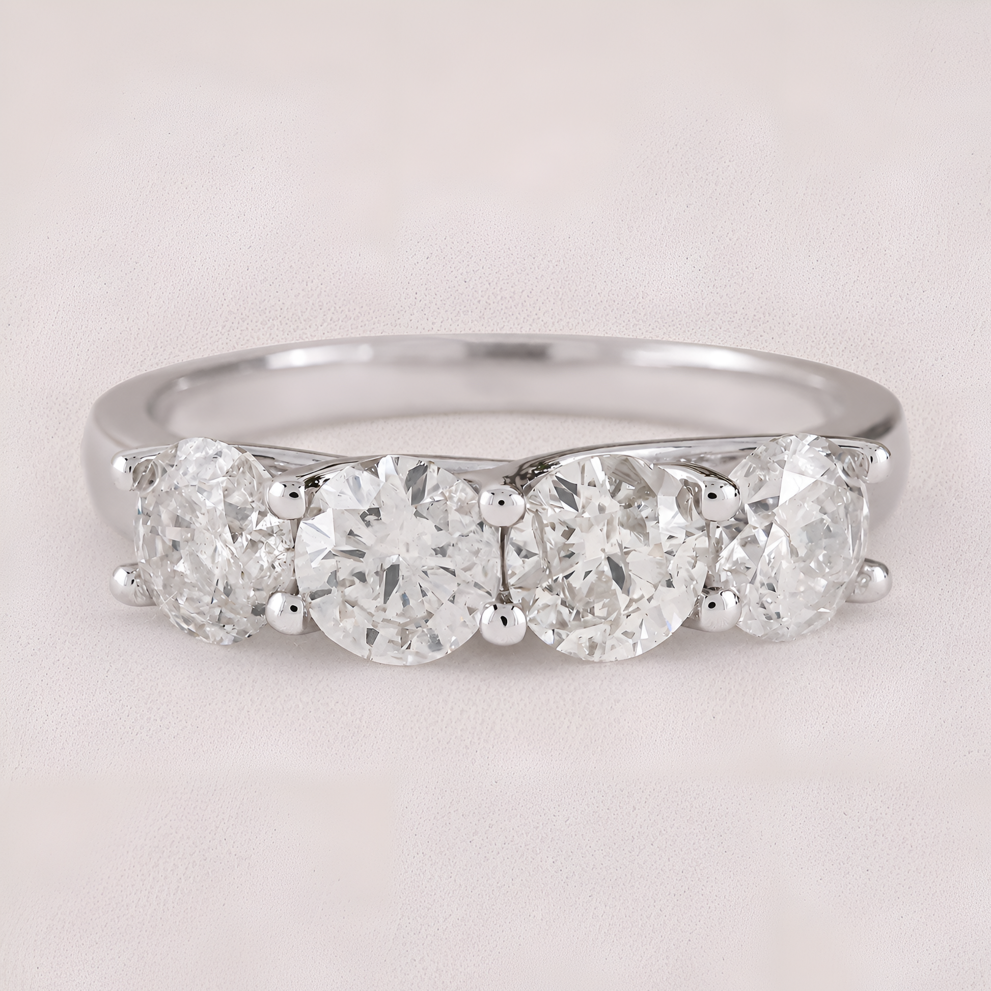 A three-stone diamond ring with round-cut diamonds set in a polished silver-colored band, shown on a light beige textured background.