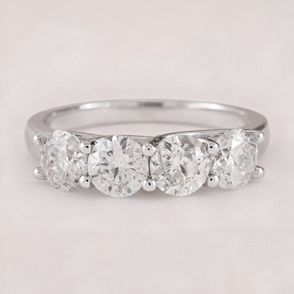 A three-stone diamond ring with round-cut diamonds set in a polished silver-colored band, shown on a light beige textured background.