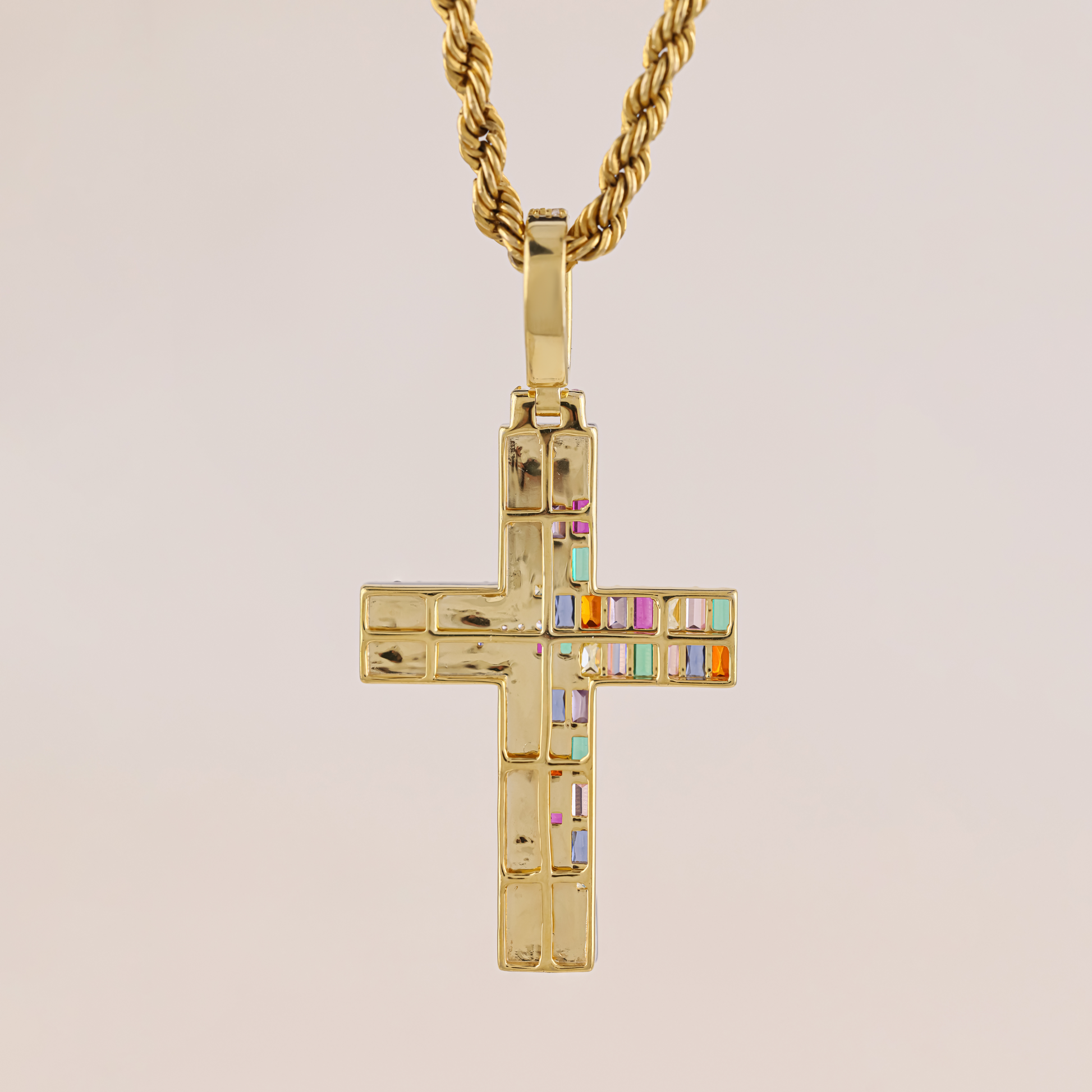 Gold cross pendant with colorful stones on a beige background