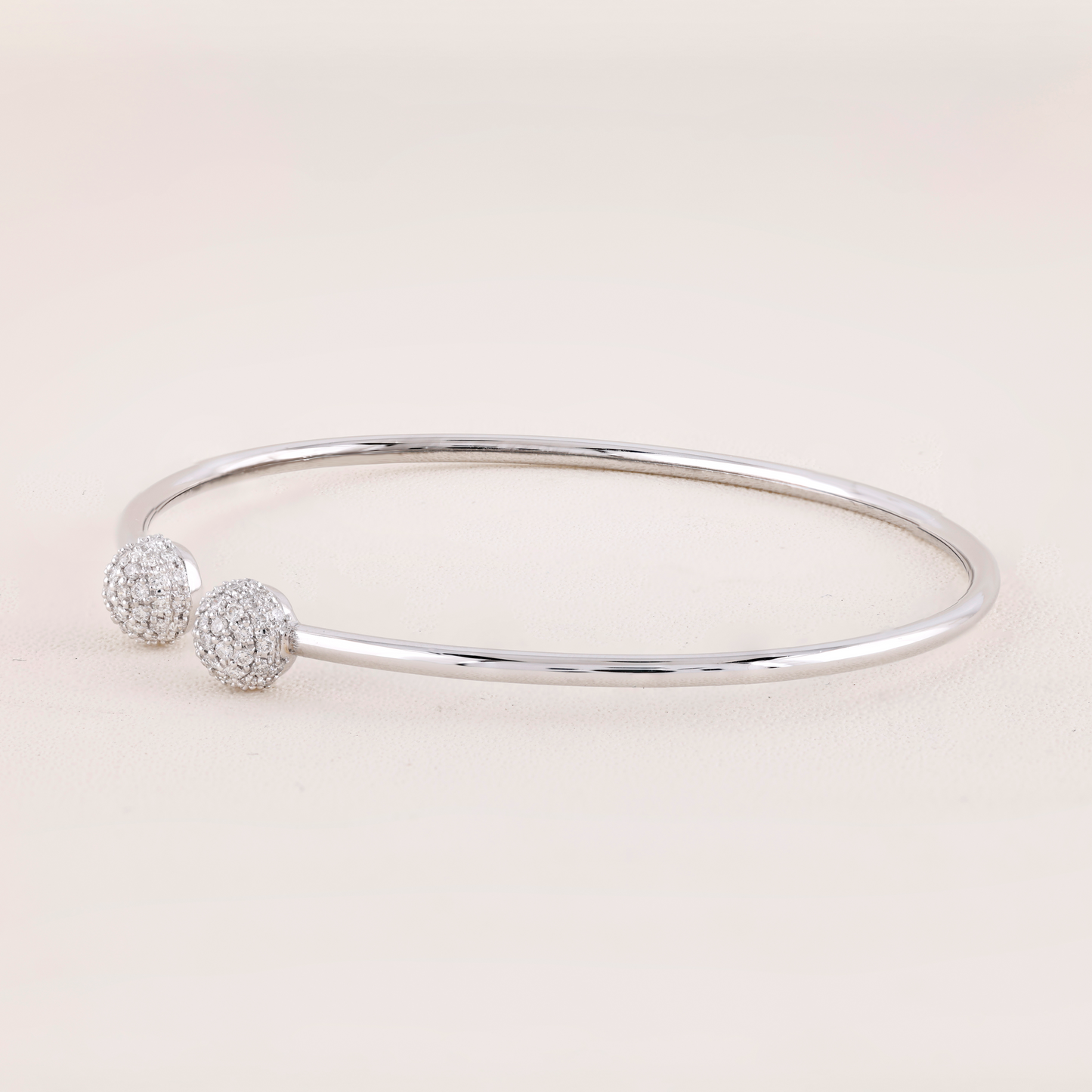 Silver bangle with two round, diamond-studded charms on a light pink background