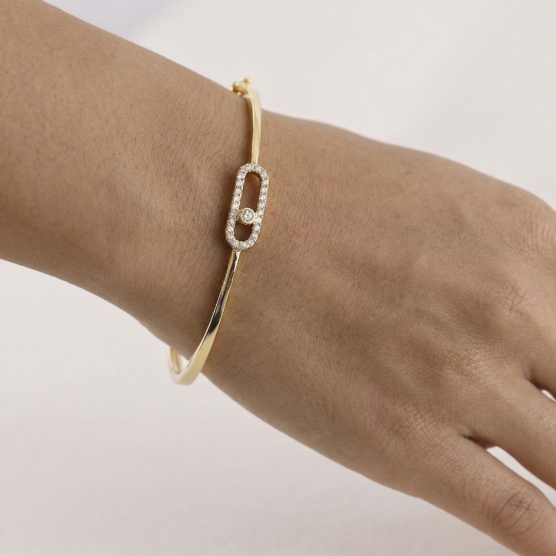 Gold bracelet with a diamond on a wrist against a light background