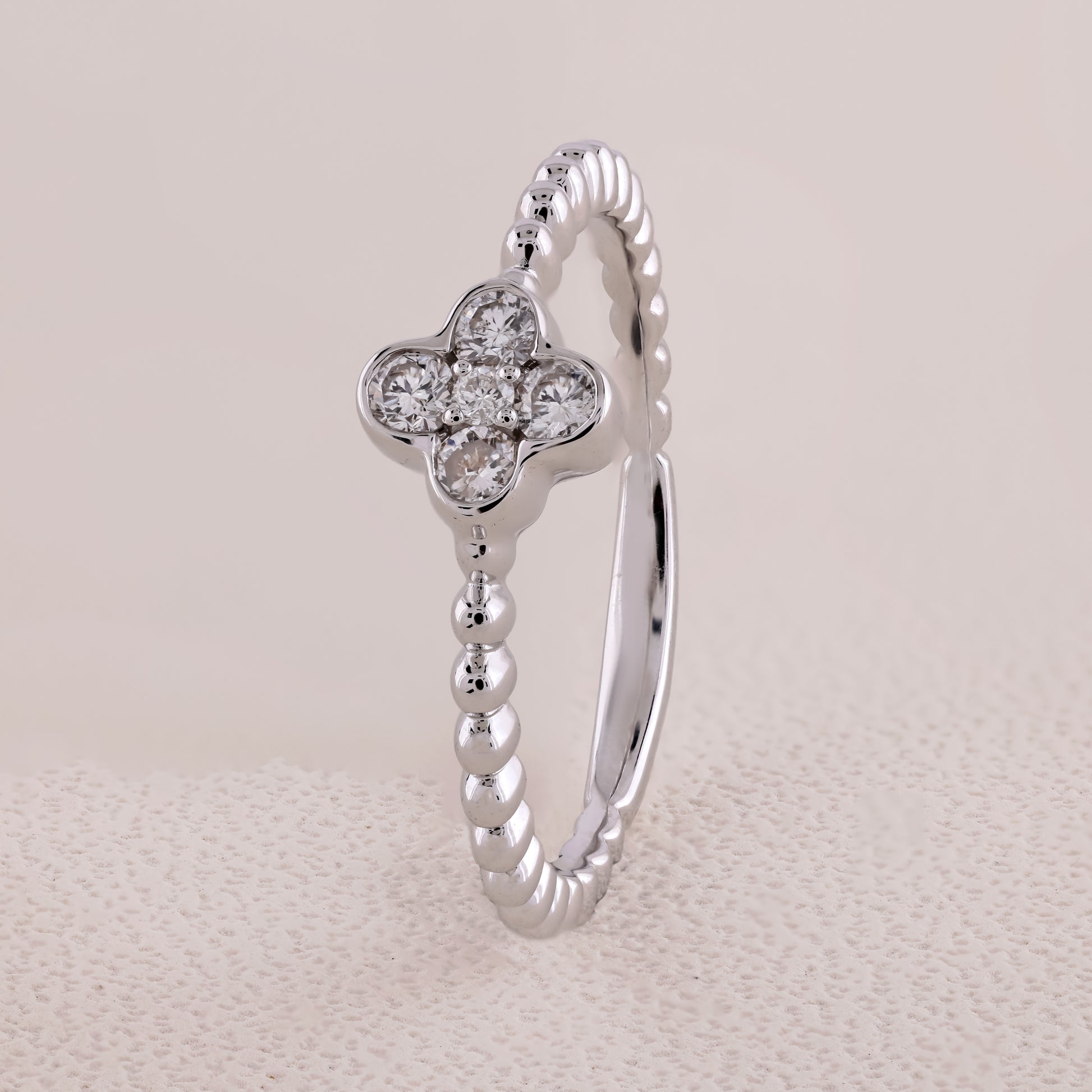 Silver ring with a clover-shaped diamond design on a beige background