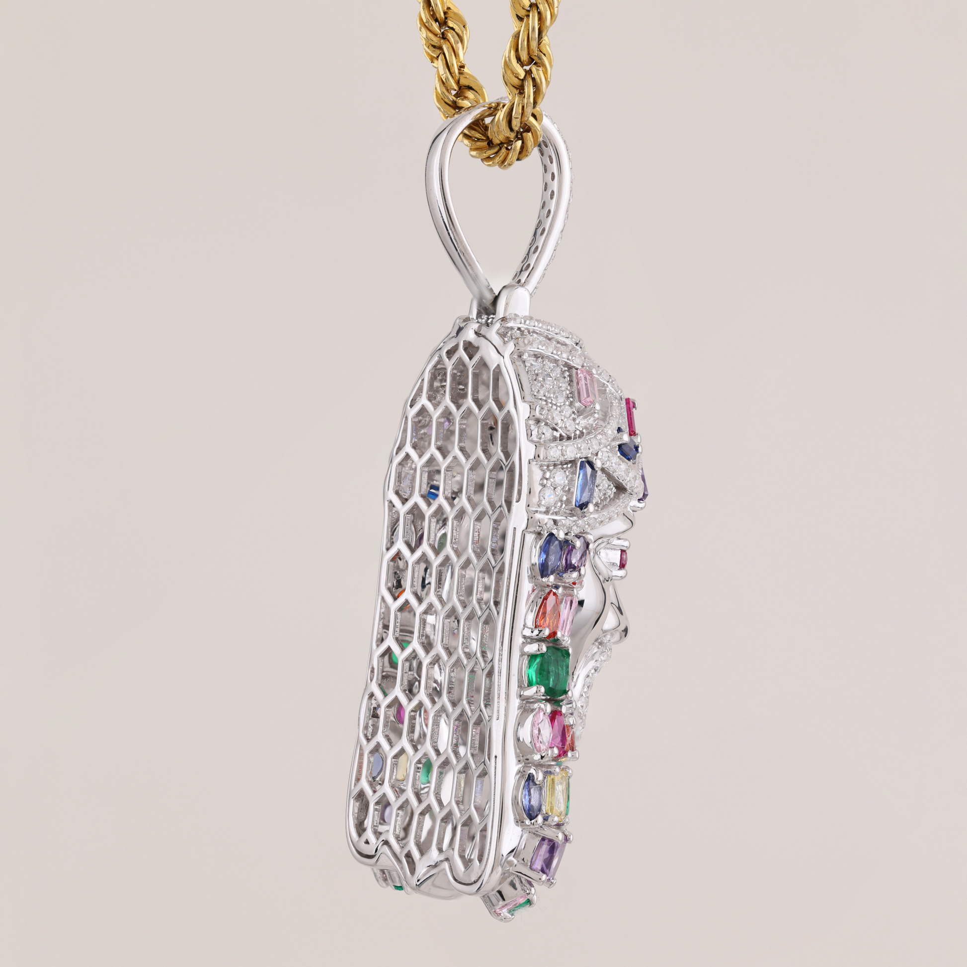 Silver pendant with colorful gemstones on a gold chain against a beige background