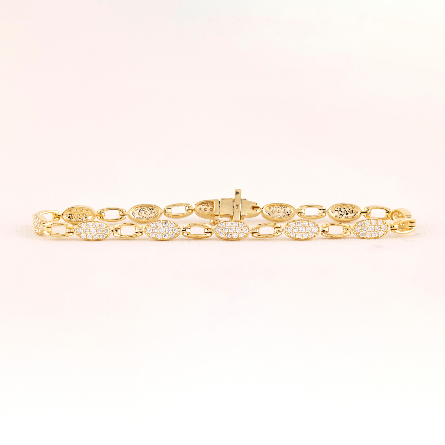 Gold bracelet with diamond accents on a light pink background