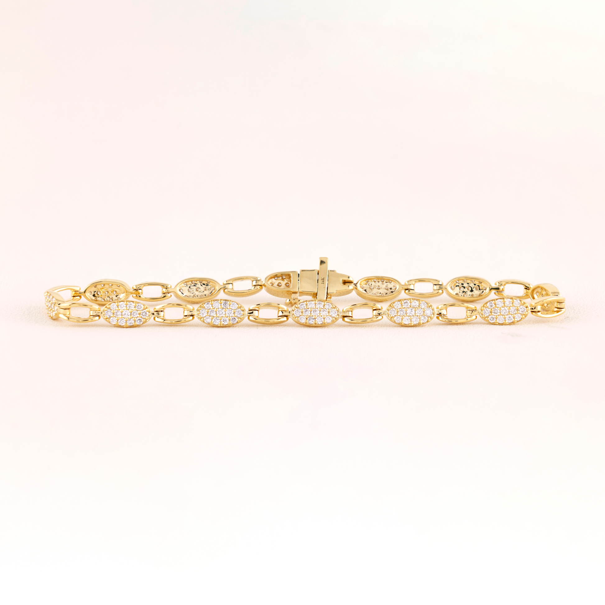 Gold bracelet with diamond accents on a light pink background