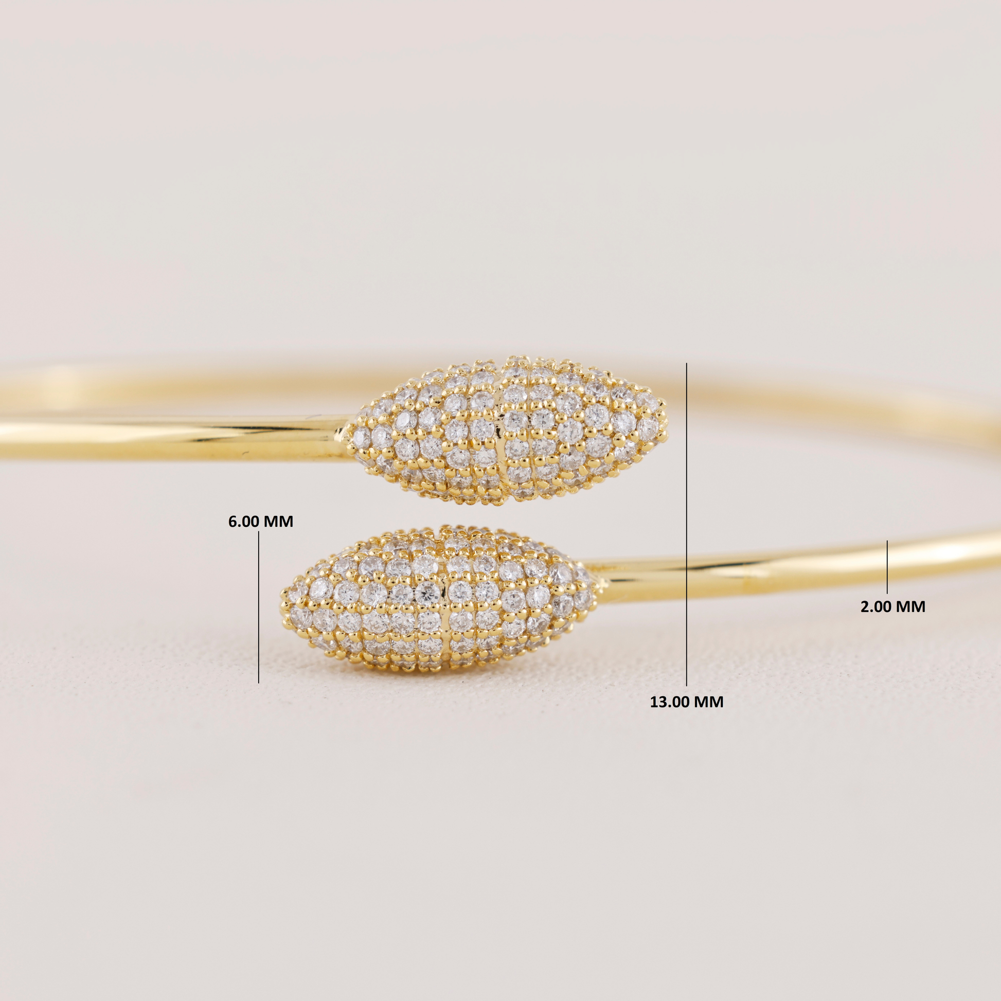 Gold bangles with diamond accents and measurements on a light background