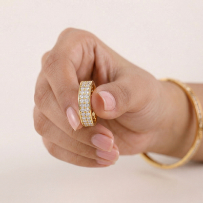 Hand wearing a gold ring with gemstones on a light background