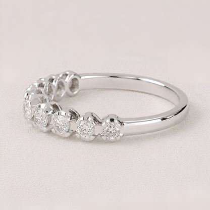 A silver diamond eternity ring featuring a row of round-cut diamonds in a halo setting on a polished band, photographed on a light beige textured background.