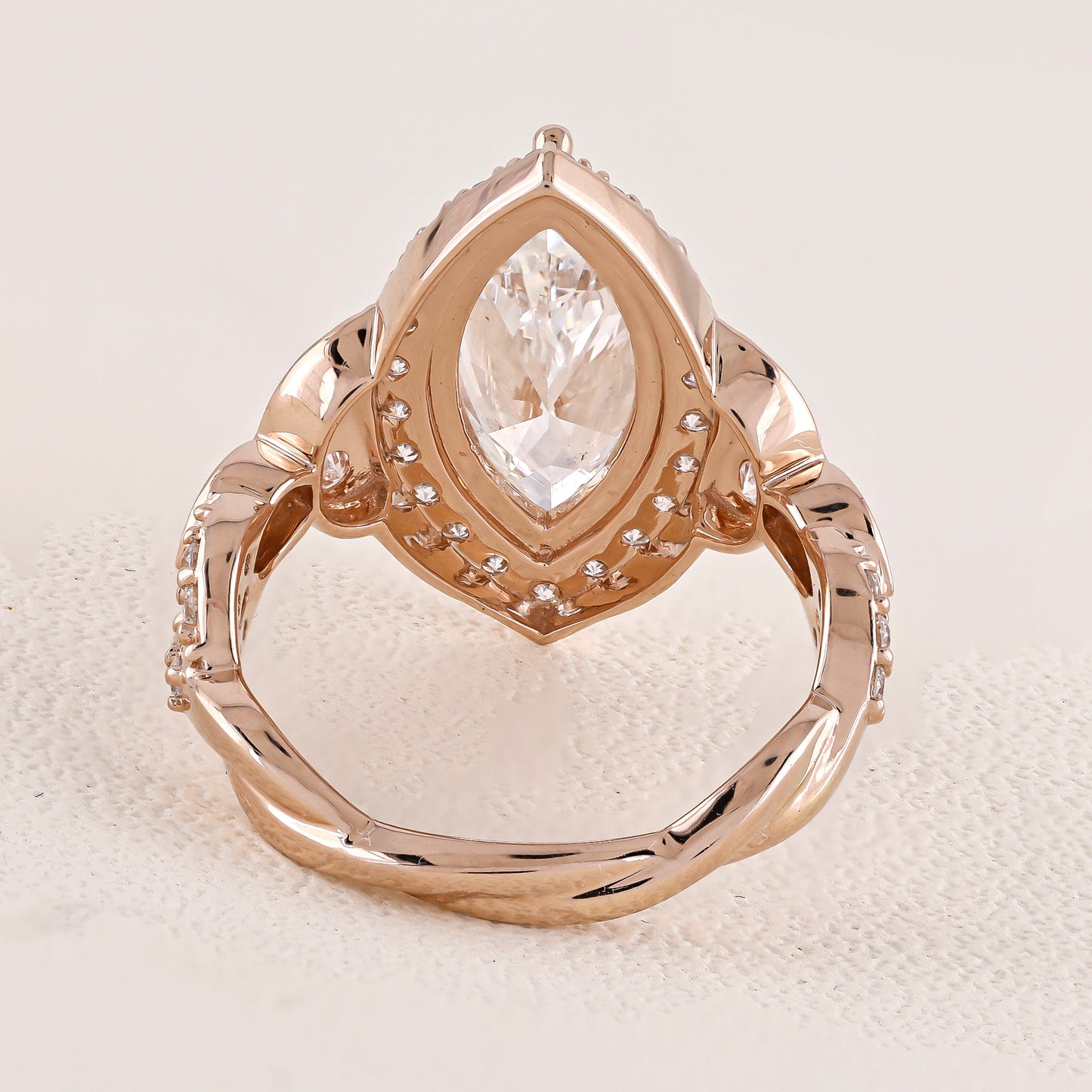 Rose gold ring with a pear-shaped diamond on a textured beige surface