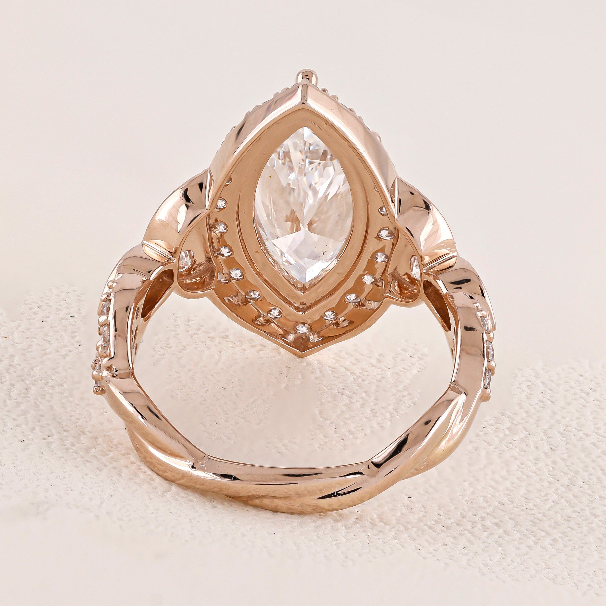 Rose gold ring with a pear-shaped diamond on a textured beige surface