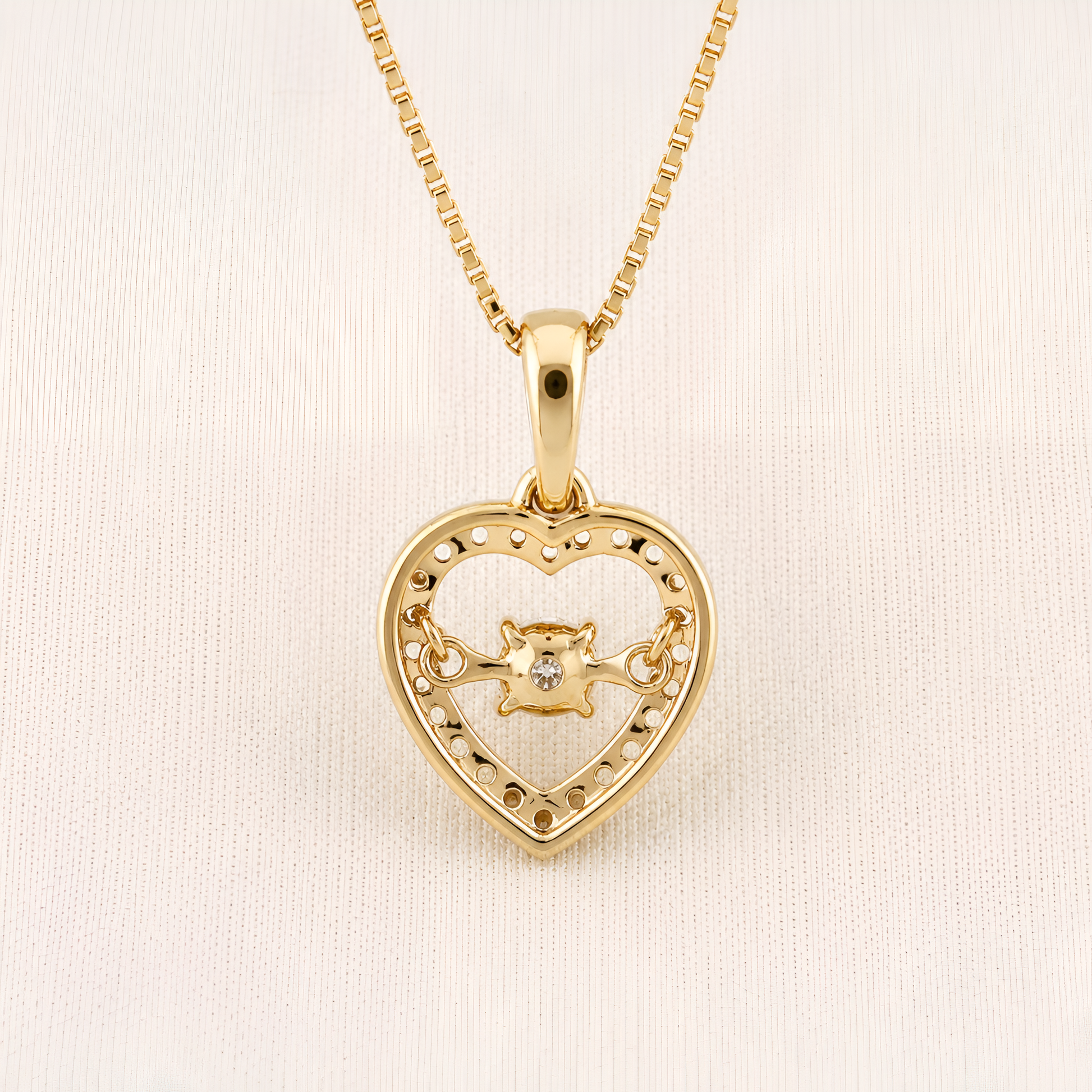 A gold heart-shaped pendant necklace with a small central lion motif, displayed on a textured off-white background.