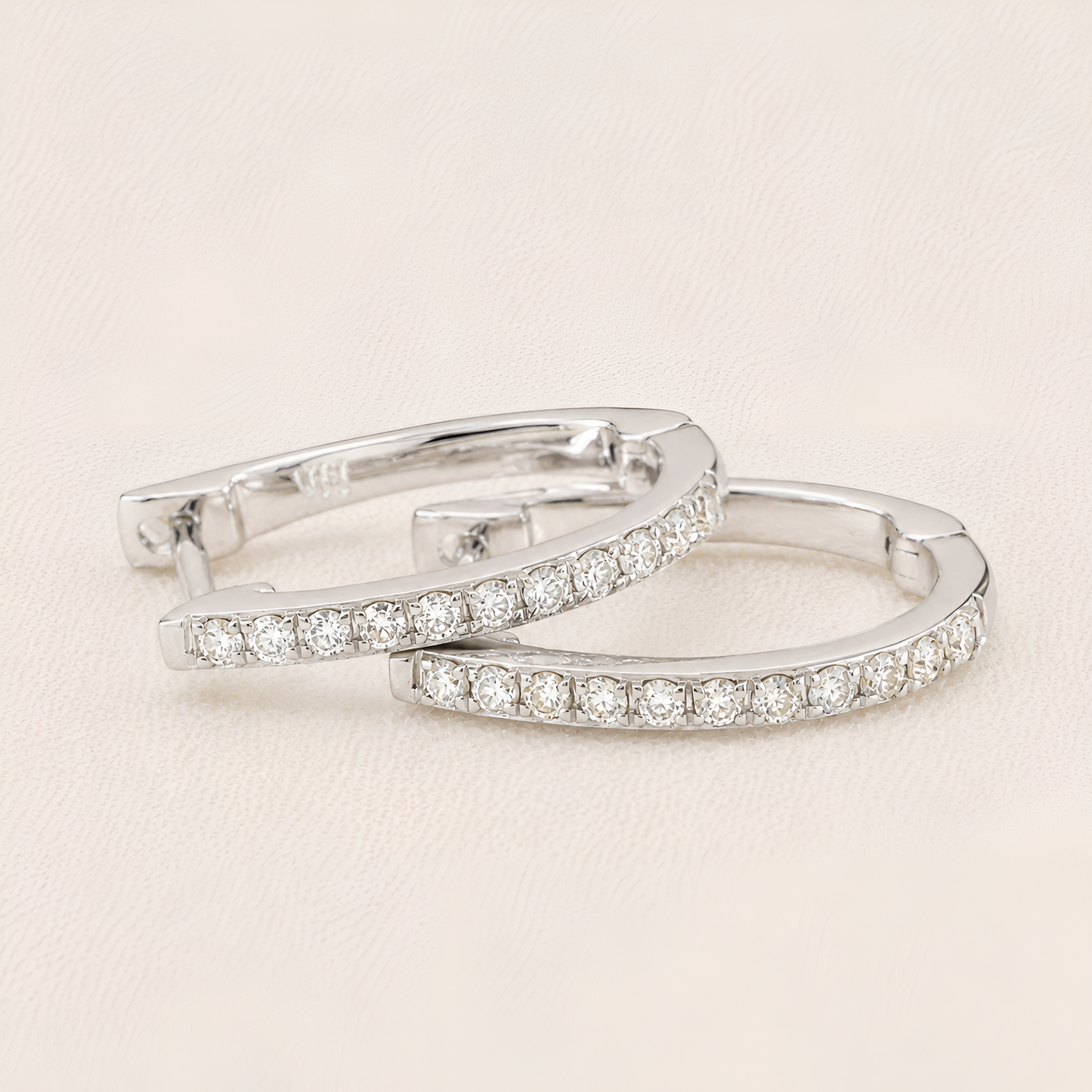 Pair of silver hoop earrings with clear gemstones on a light beige background