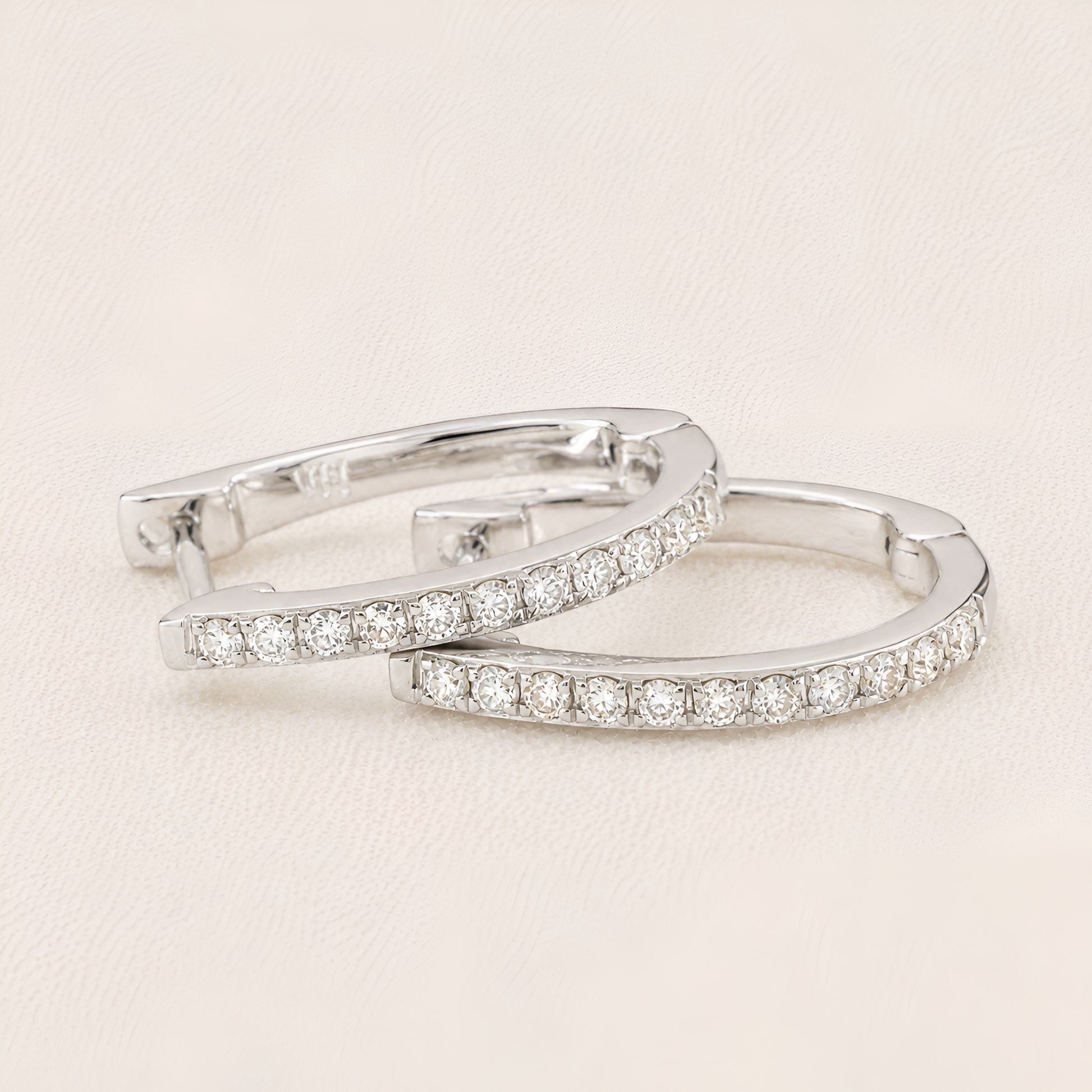 Pair of silver hoop earrings with clear gemstones on a light beige background
