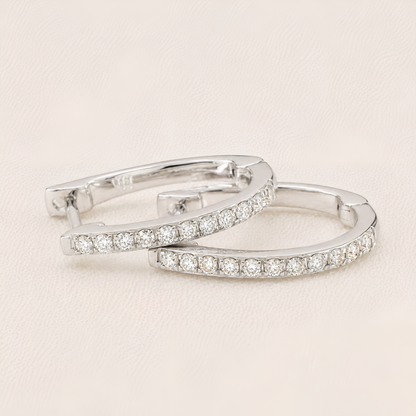Pair of silver hoop earrings with clear gemstones on a light beige background