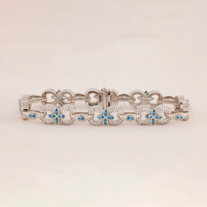 Silver bracelet with floral designs and blue stones on a light beige background