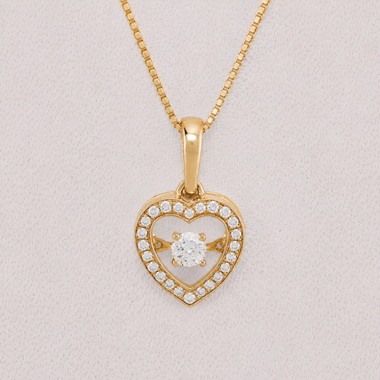 A yellow gold heart-shaped pendant necklace with a central round-cut clear gemstone and a border of small pavé-set clear stones, shown on a textured light pink background.