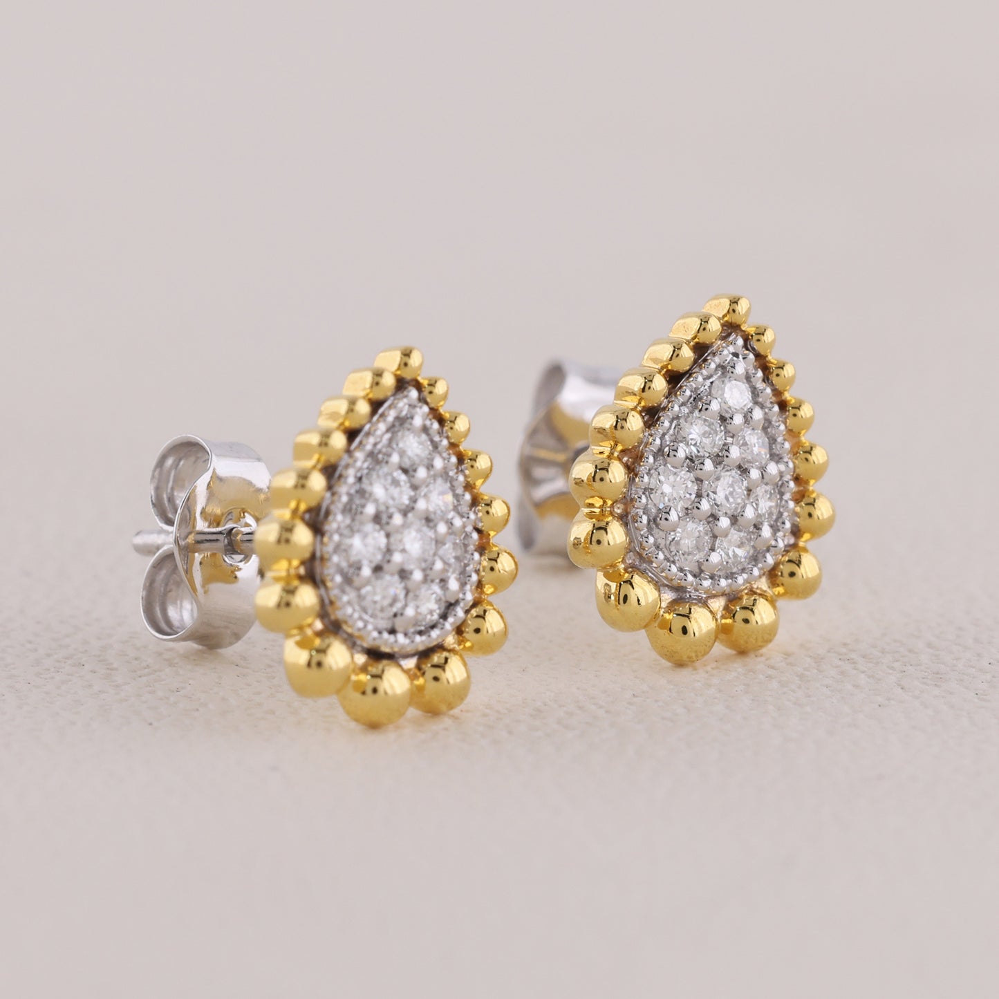 Pair of gold and silver teardrop-shaped earrings on a light gray background