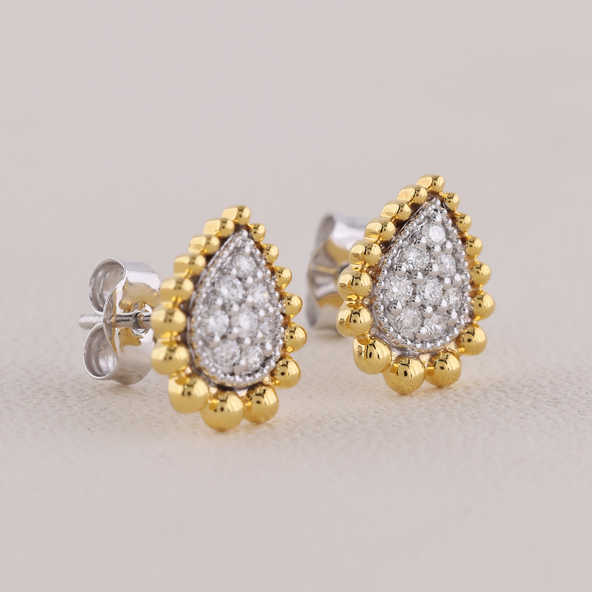 Pair of gold and silver teardrop-shaped earrings on a light gray background