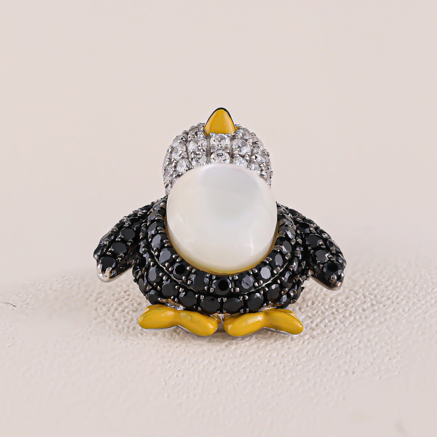 Penguin-shaped brooch with gemstones on a beige background