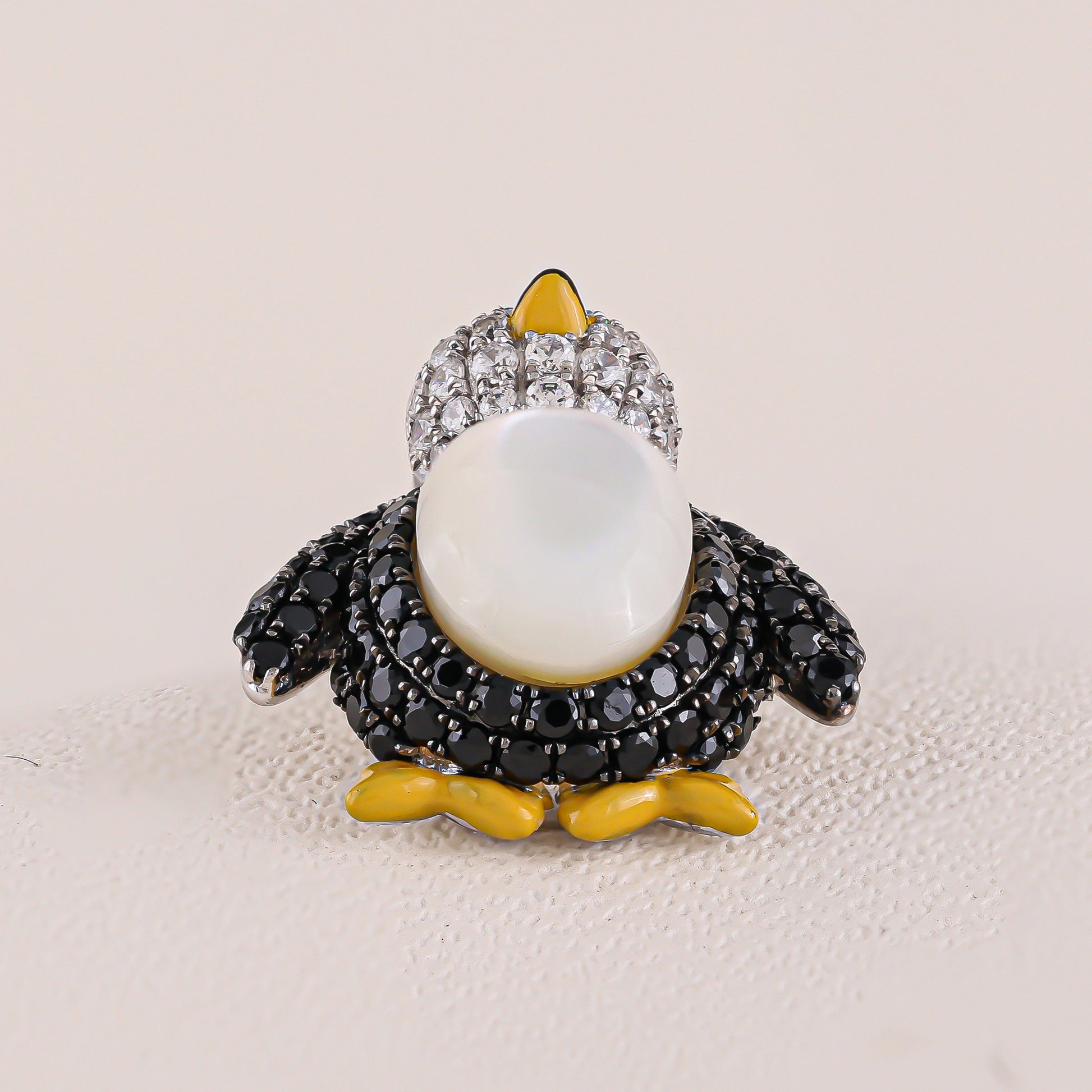 Penguin-shaped brooch with gemstones on a beige background