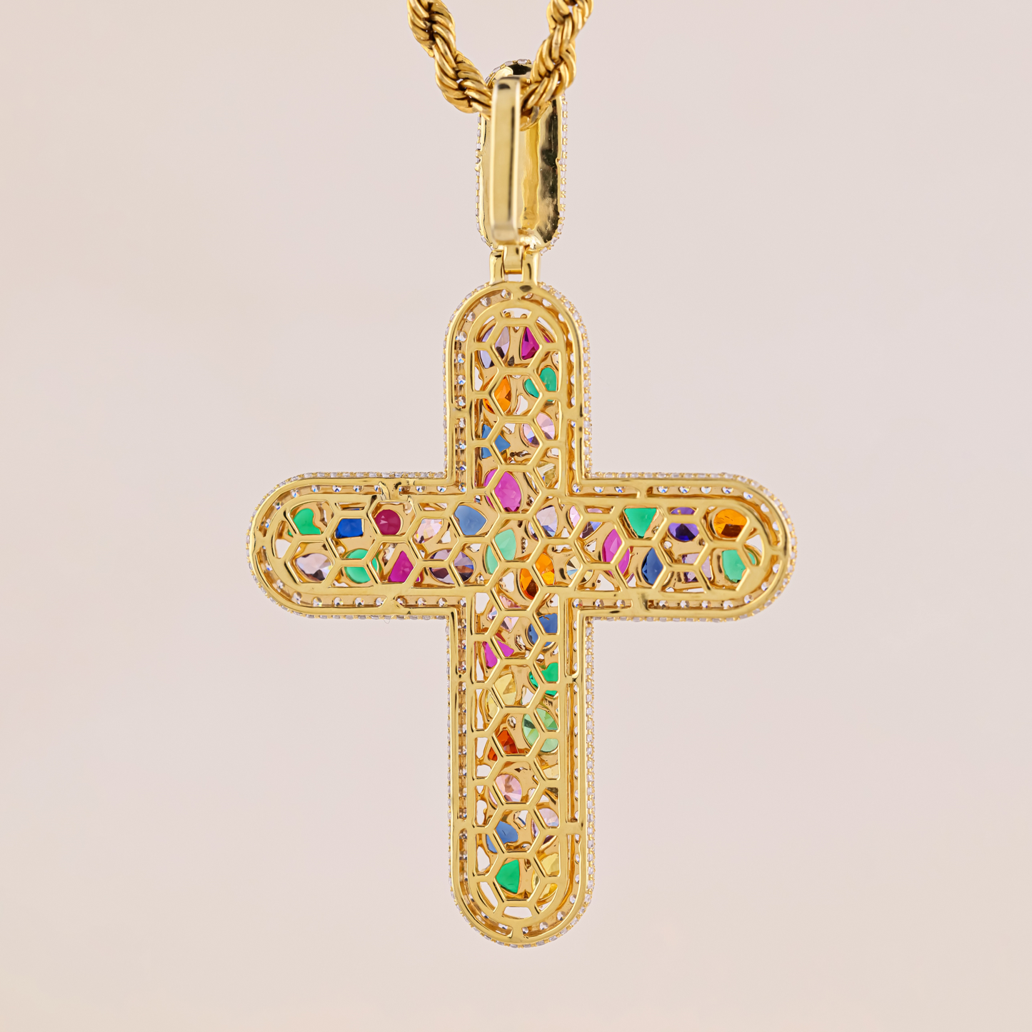 Gold cross pendant with colorful gemstones on a beige background