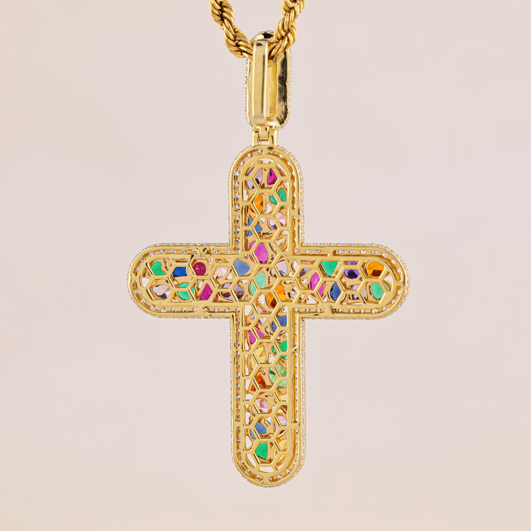 Gold cross pendant with colorful gemstones on a beige background