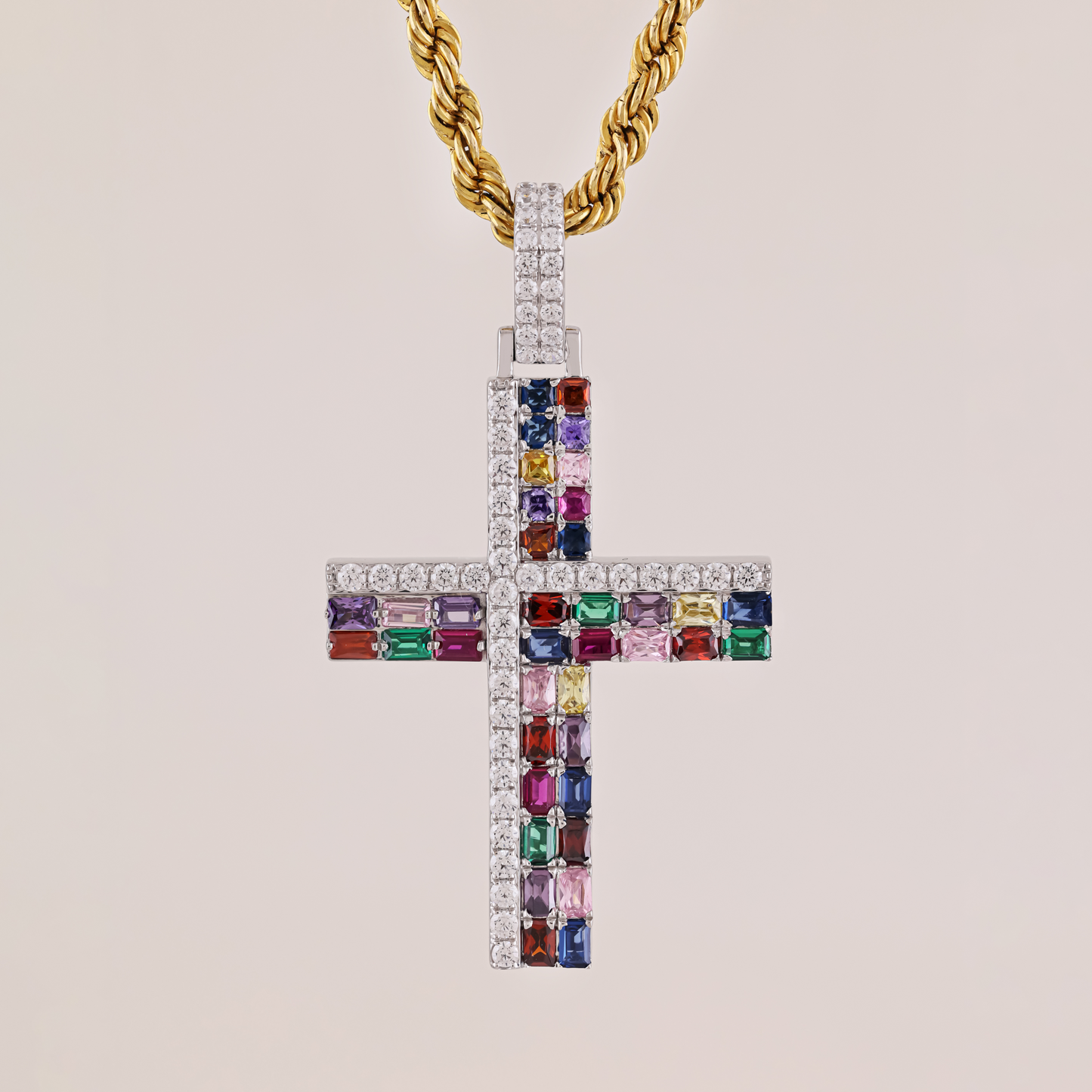 Cross-shaped pendant with colorful gemstones and a gold chain on a beige background