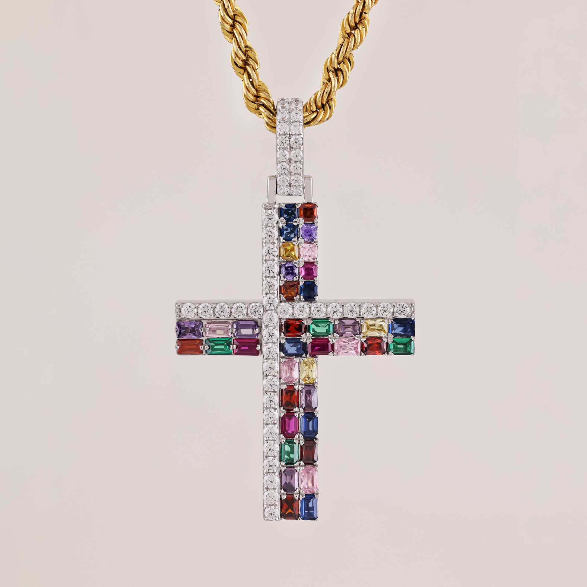 Cross-shaped pendant with colorful gemstones and a gold chain on a beige background