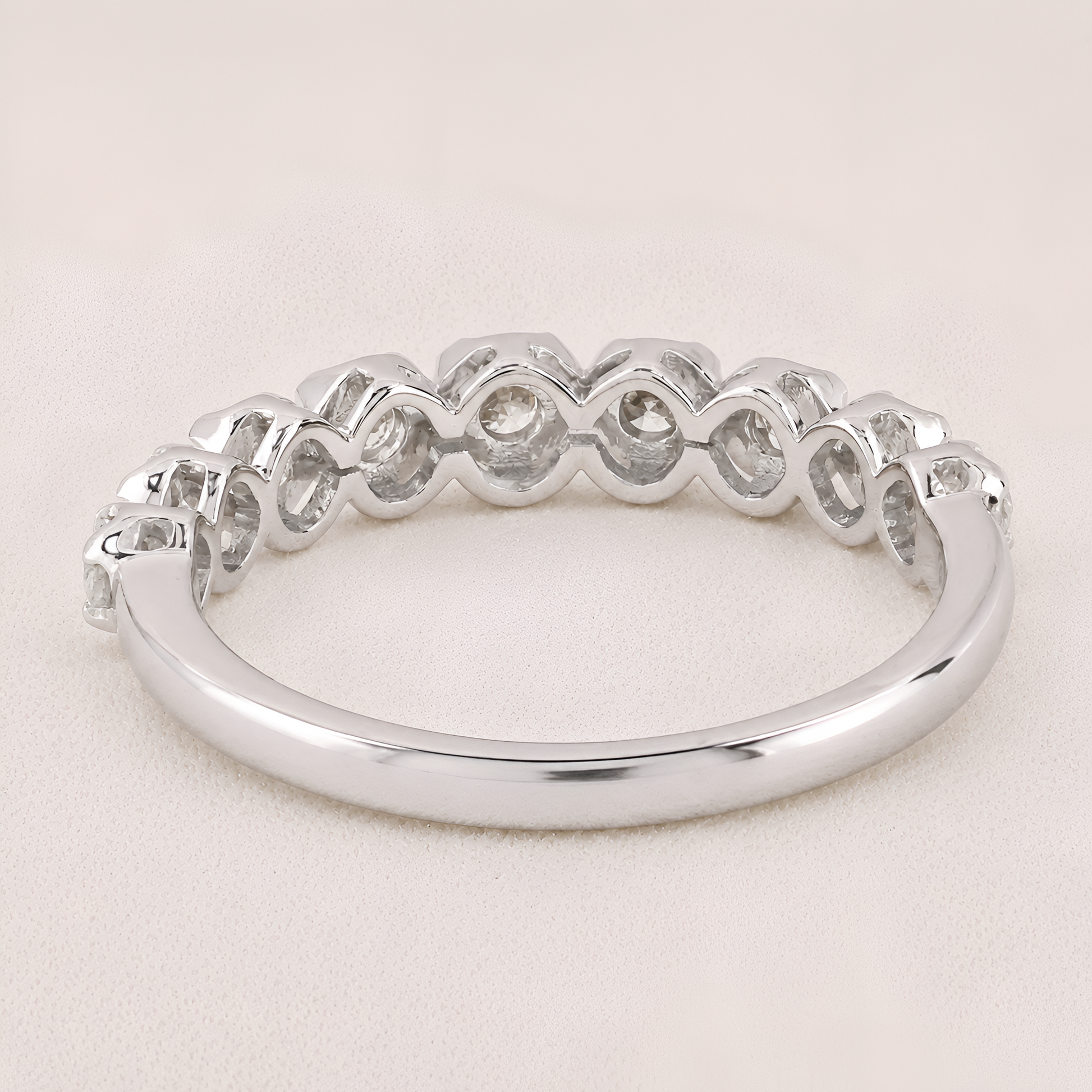 A silver band ring featuring a row of small, bezel-set clear gemstones in a repeating wavy pattern, shown on a light beige textured background.