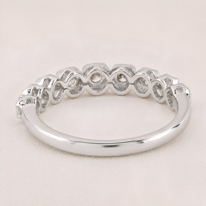 A silver band ring featuring a row of small, bezel-set clear gemstones in a repeating wavy pattern, shown on a light beige textured background.
