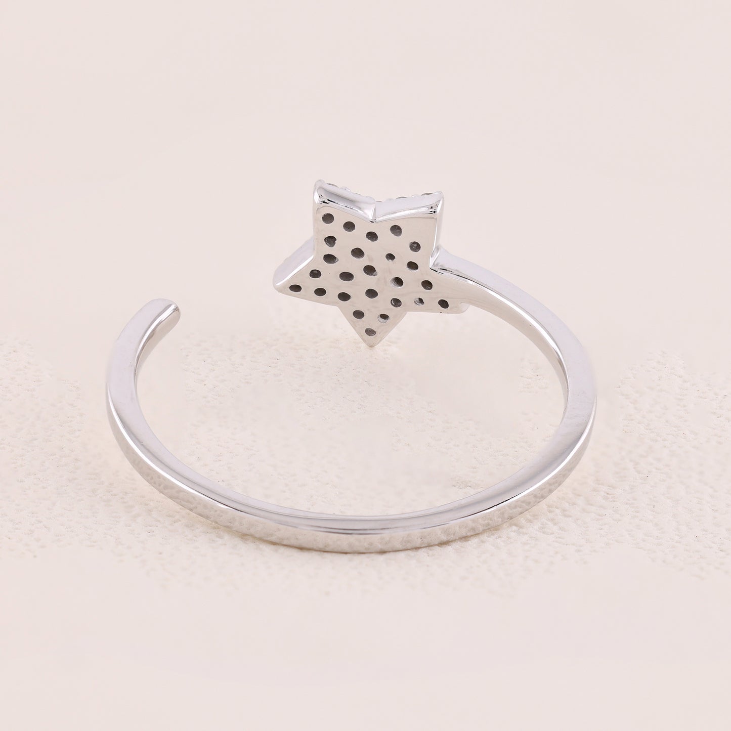 Silver ring with a star-shaped top on a beige background