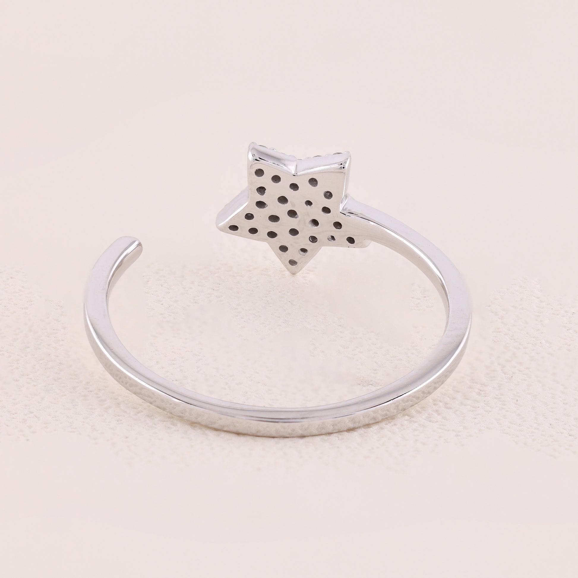 Silver ring with a star-shaped top on a beige background
