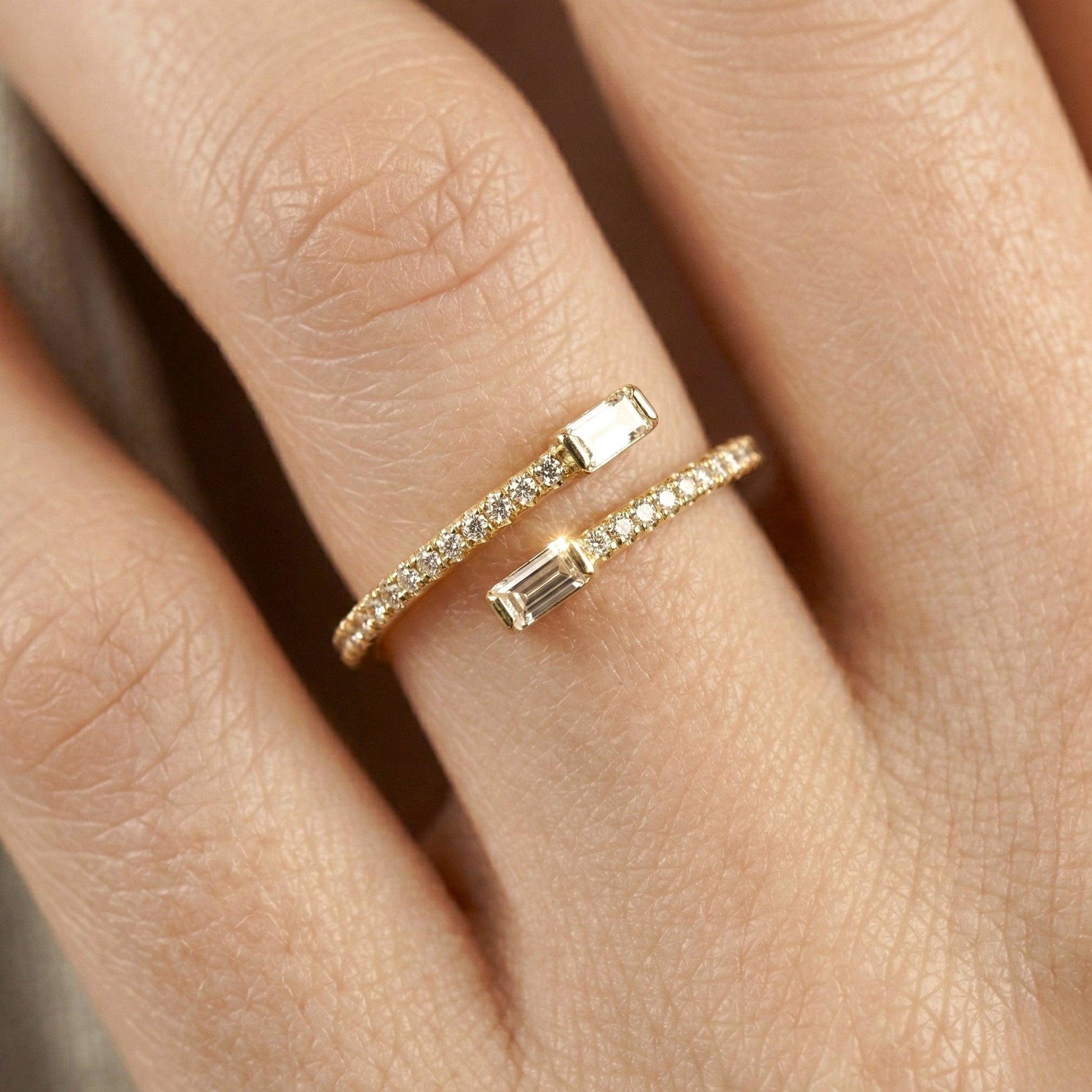 Close-up of a hand wearing two gold rings with gemstones on a neutral background
