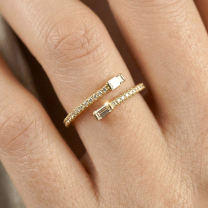Close-up of a hand wearing two gold rings with gemstones on a neutral background