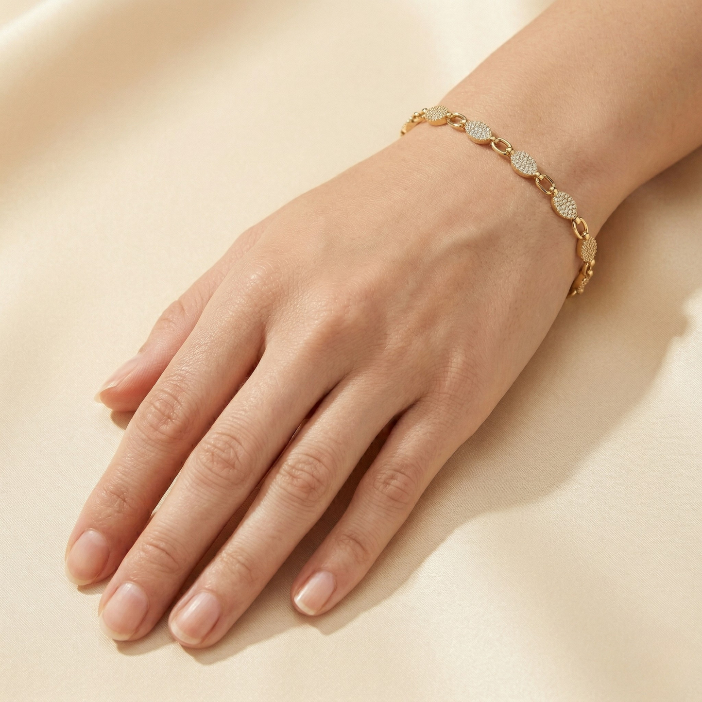 Gold bracelet on a hand against a beige background