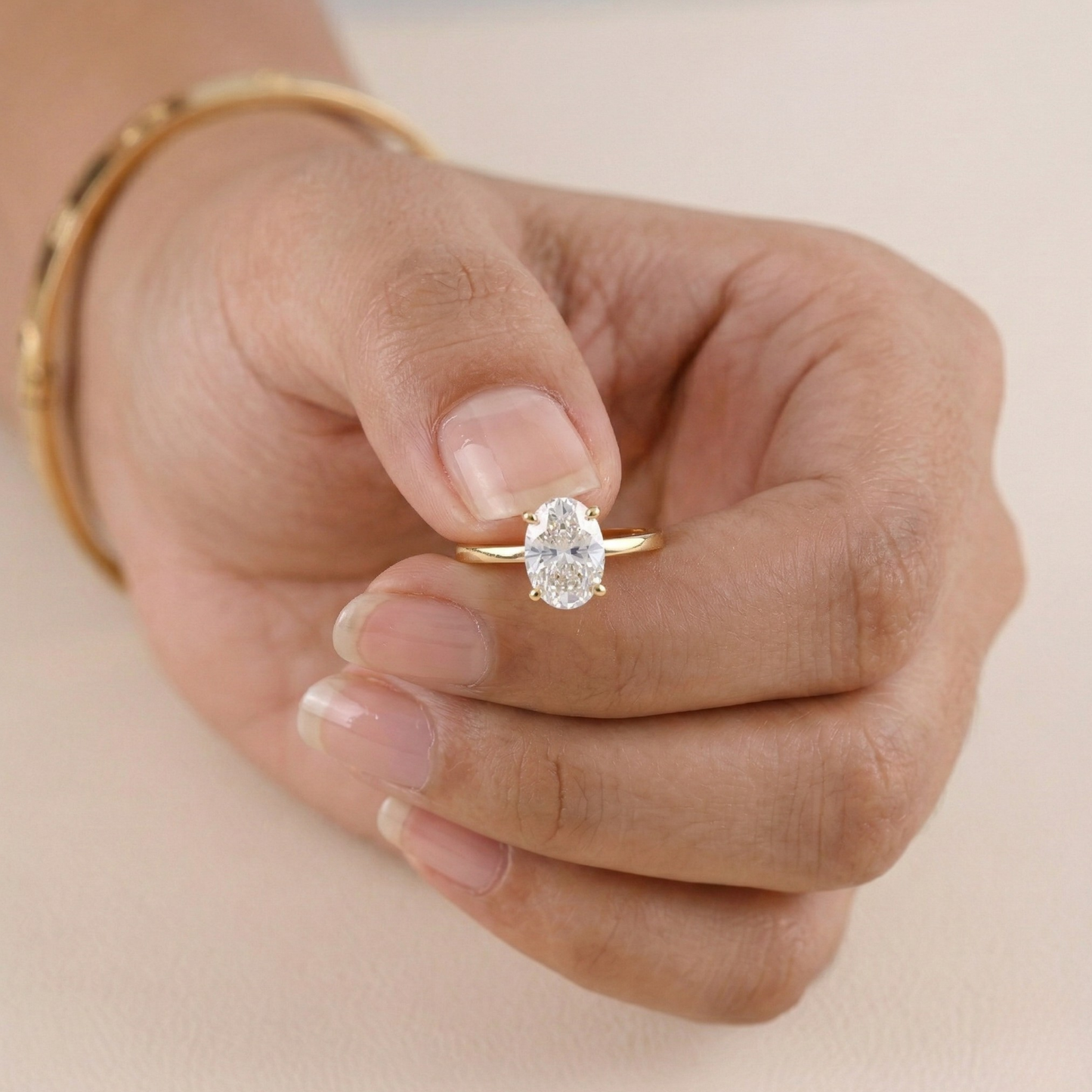 Gold ring with a diamond on a hand against a beige background