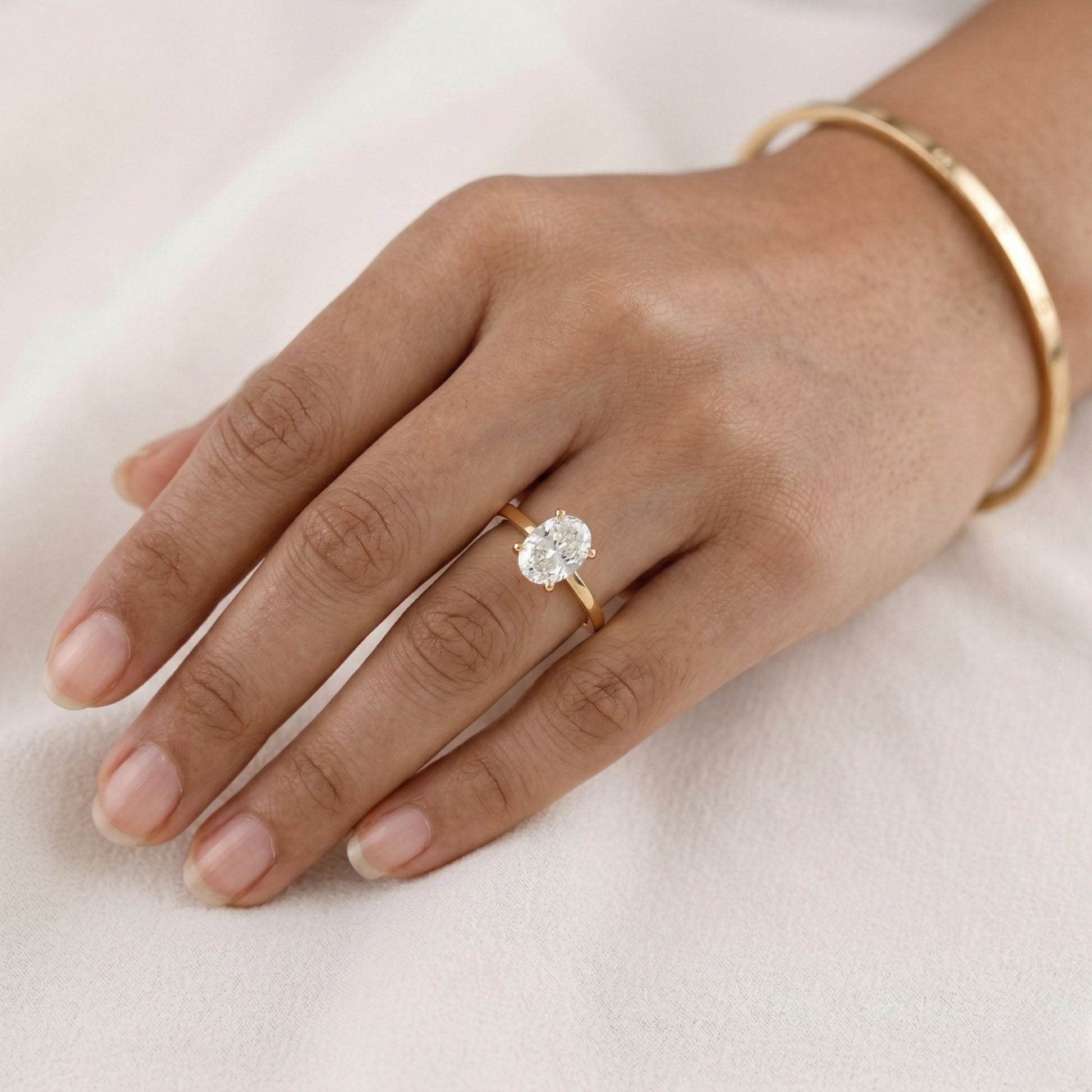 Hand wearing a gold ring with a diamond on a light background