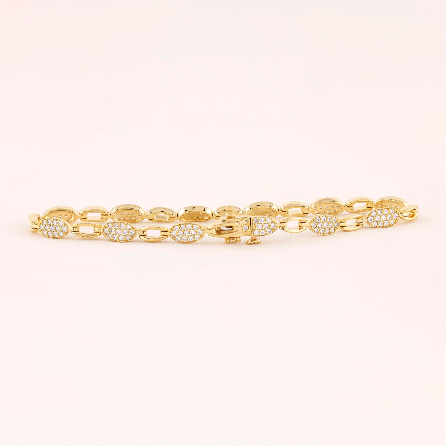 Gold bracelet with diamond accents on a light pink background