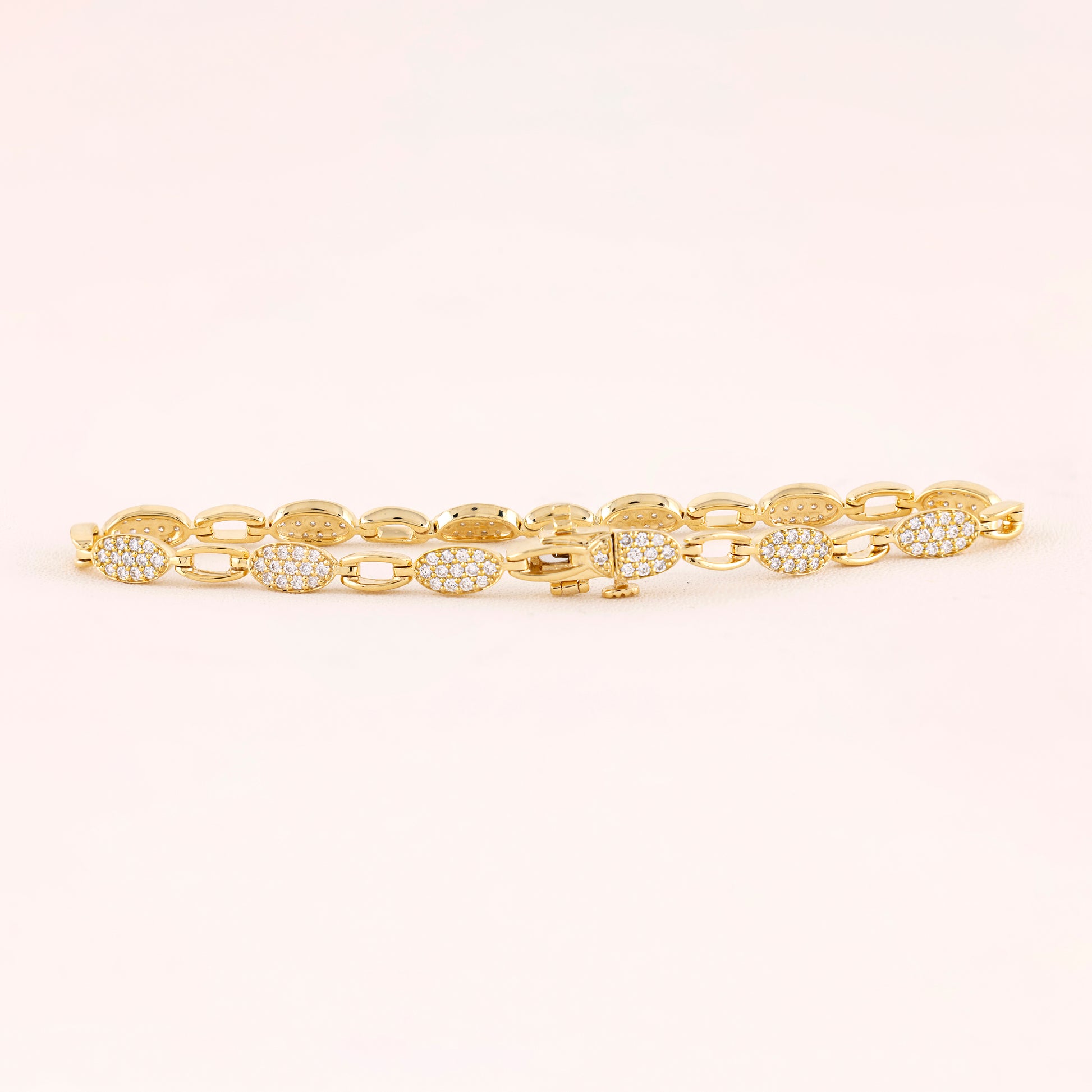 Gold bracelet with diamond accents on a light pink background