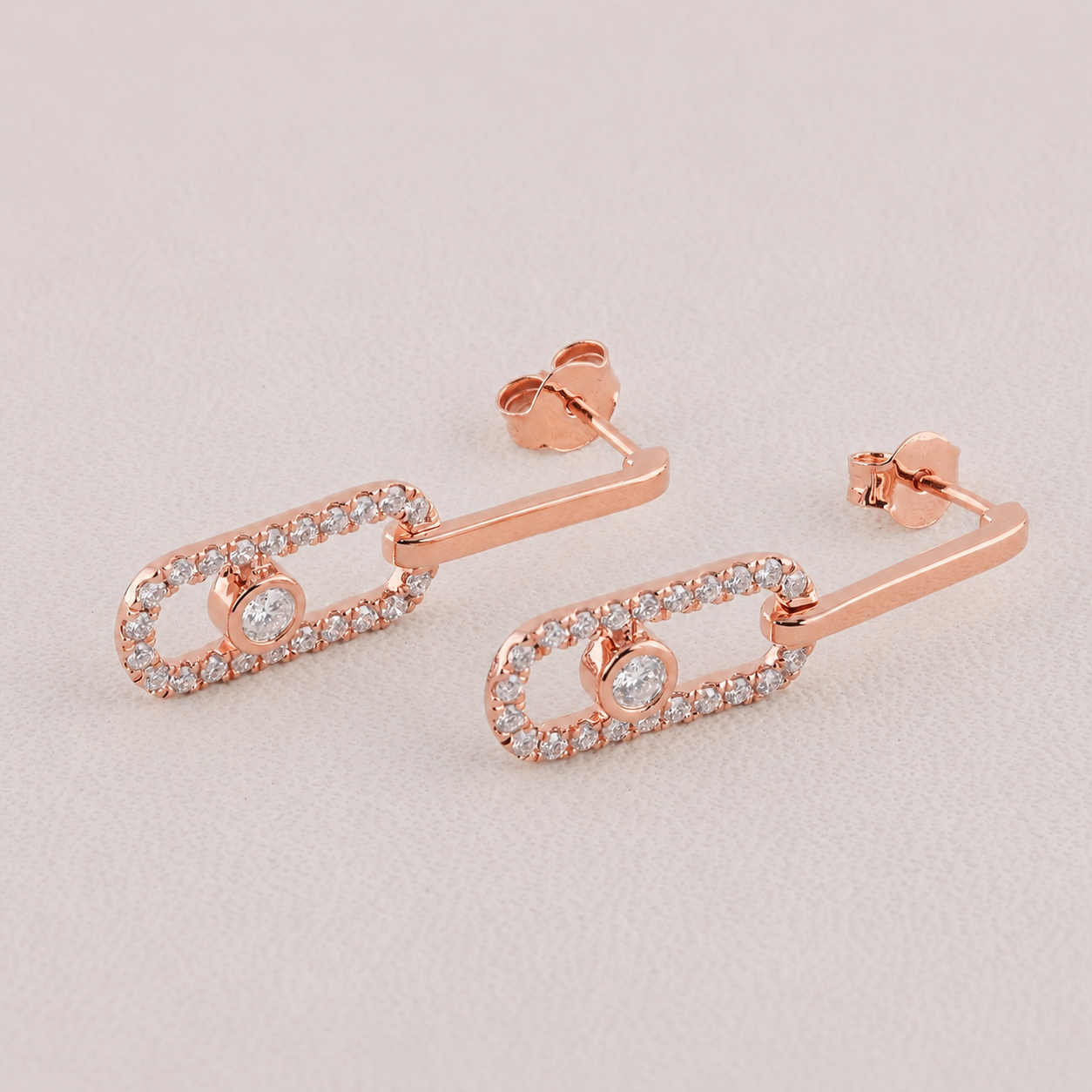 Rose gold earrings with clear gemstones on a light gray background