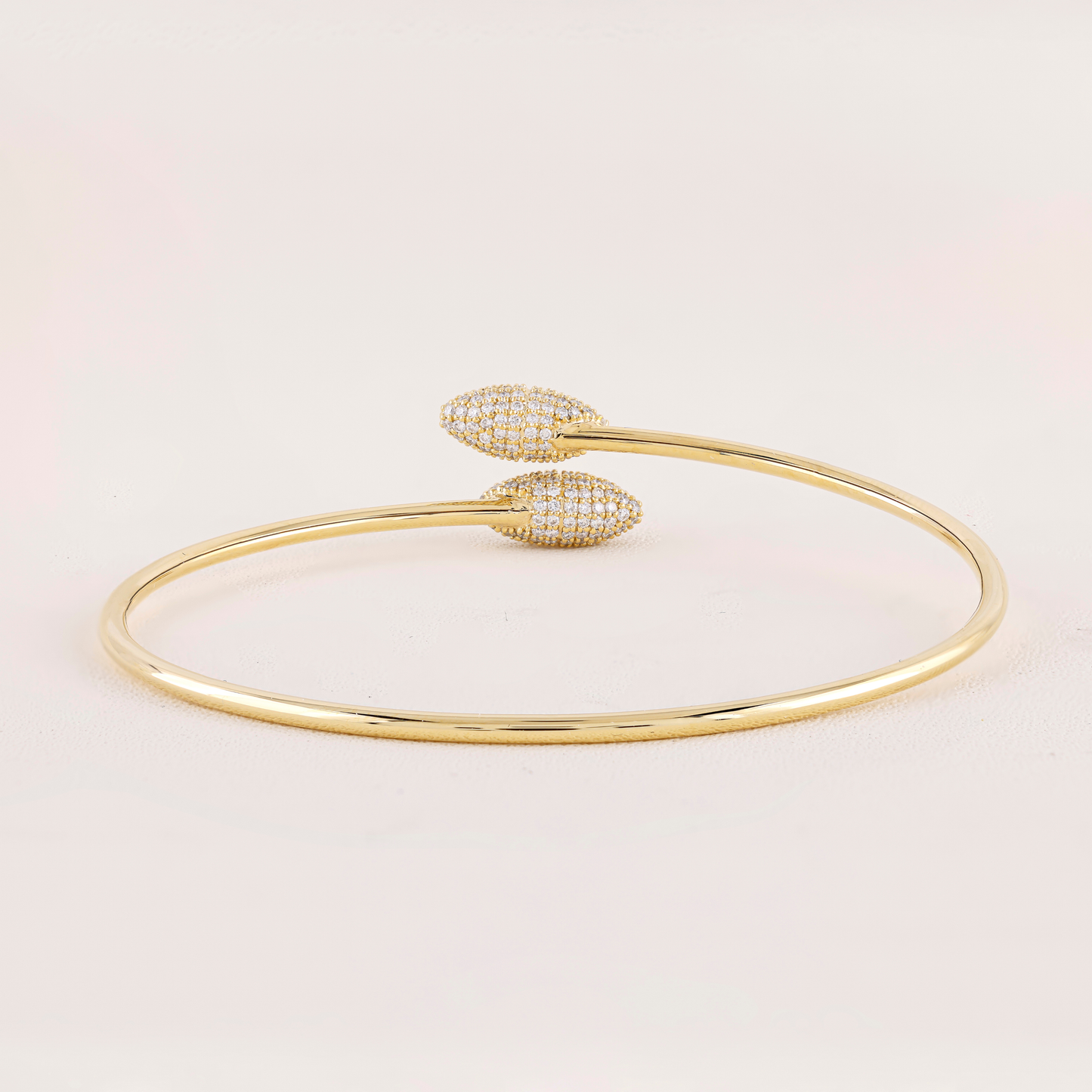 Gold bracelet with heart-shaped ends on a light pink background