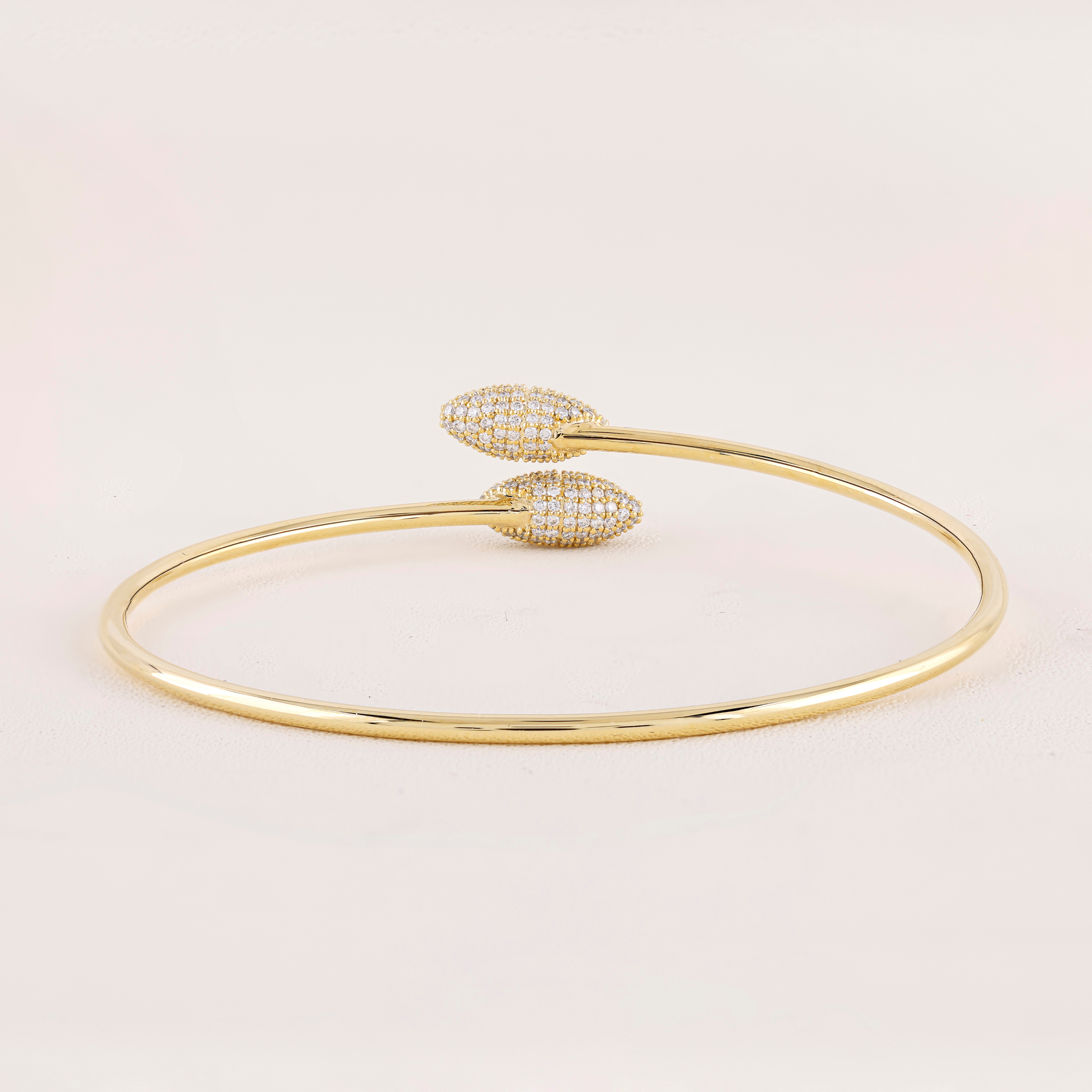 Gold bracelet with heart-shaped ends on a light pink background