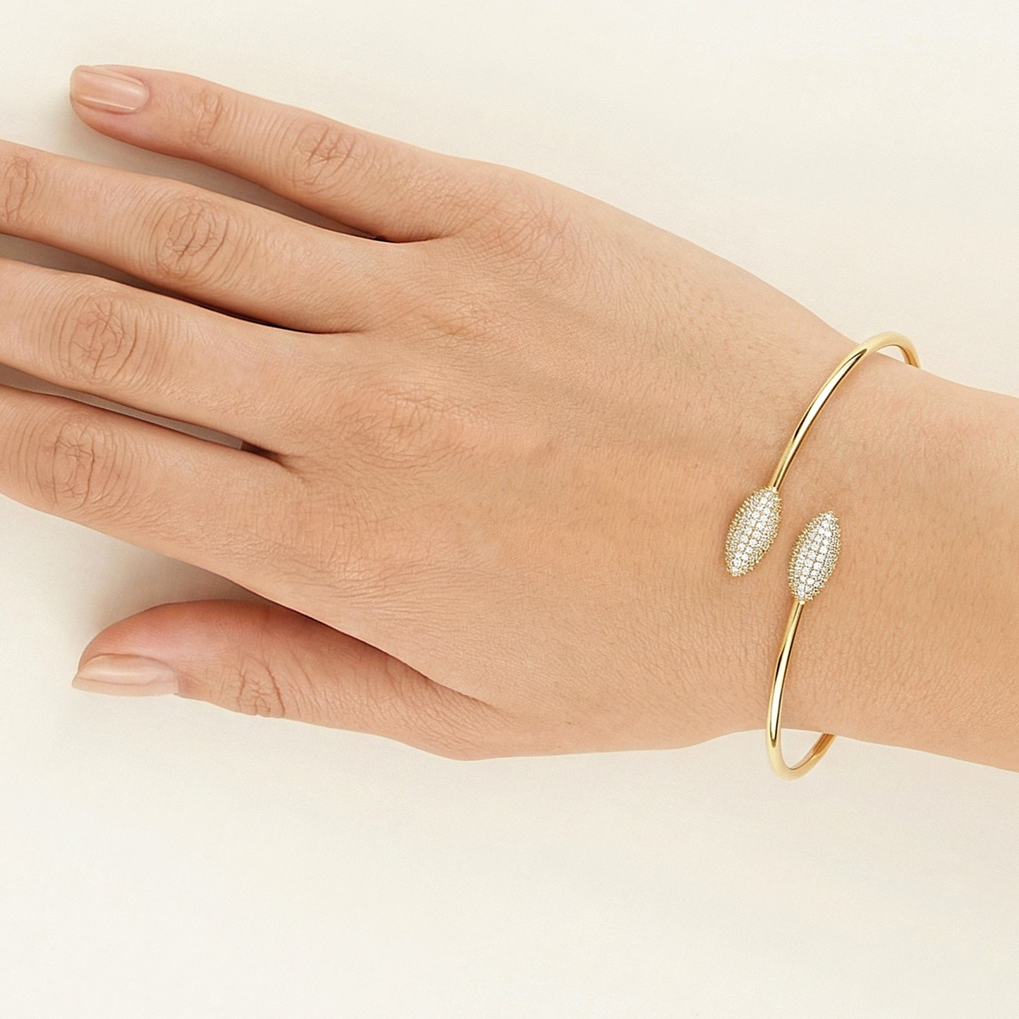 Gold bracelet with leaf-like designs on a hand against a beige background